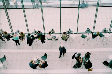 Des personnes dans un hall, certaines passent, certaines sont assises à des tables